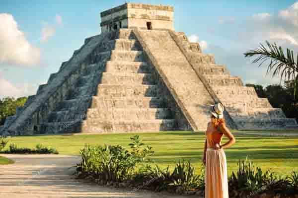 Girl tourist in a hat stands near the pyramid in Chichen Itza