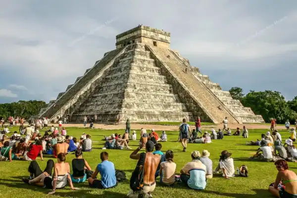 Equinox day at  Chichen Itza pyramid with people sitting on grass during tour