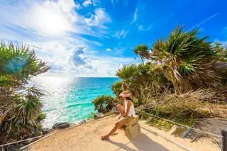 Girl seated by
  cliff at Tulum ruins