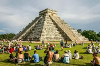 Equinox day at
  Chichen Itza pyramid with people sitting on grass during tour