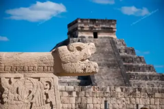 Snake head
  sculpture with Kukulkan pyramid in background